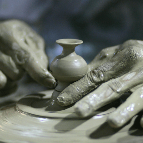 Bild på händer, täckta av lera, som drejar ett föremål.