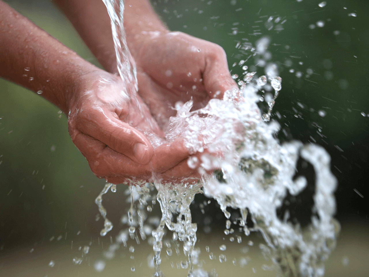 Bild på händer som hålls under ett vattenflöde. 